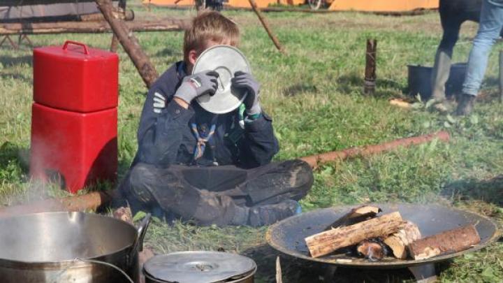 spejderdreng med røg i øjnene gemmer sig bag grydelåg